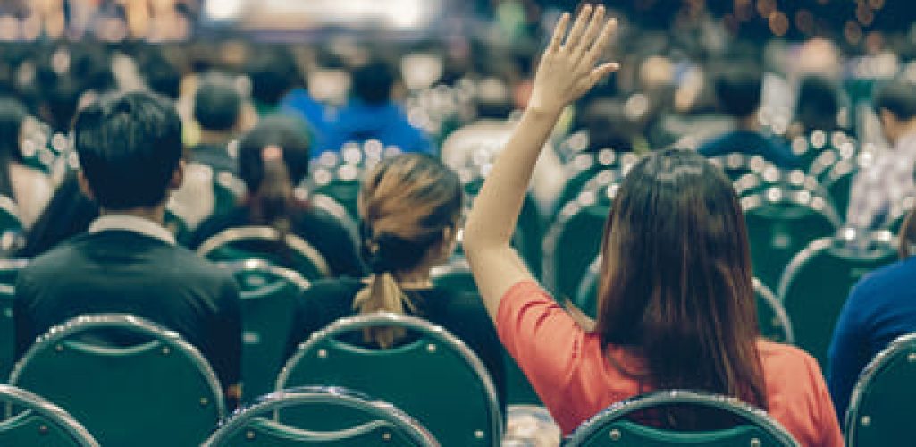 An attendee in the audience at a conference raising her hand.