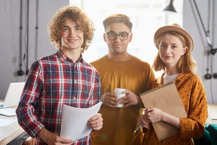 Three young successful employees in smart casual spending working day in office