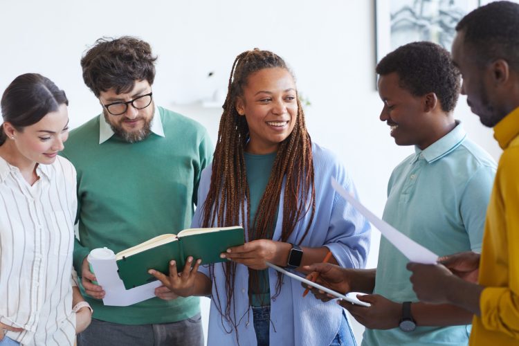 Waist up portrait of multi-ethnic business team listening to smiling African-American woman during meeting in office