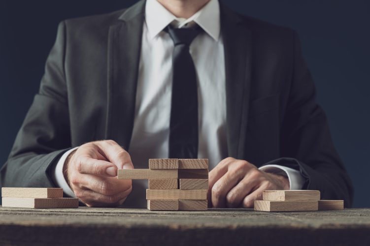 Front view of businessman at his desk making a stack of wooden pegs in a conceptual image of business strategy and idea.