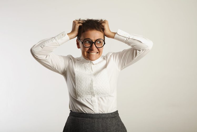 Angry female teacher in panic with teeth clenched and hands in her hair against white wall background