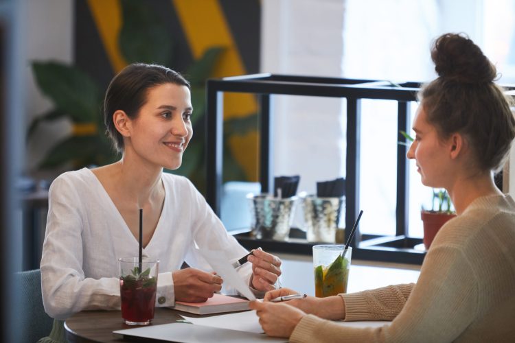 Young cheerful female agent looking at client during explanation of contract terms and discussing them at meeting