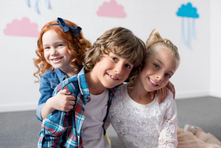 portrait of adorable happy kids smiling at camera while embracing at birthday party