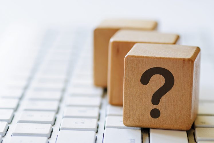 Small wooden dices with question mark on one side, sitting on computer keyboard and viewed in close-up with blurred copy space